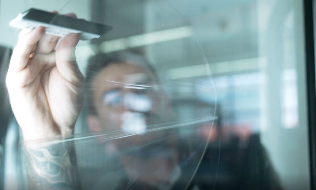 Technician inspecting transparent surface with optical measurement and testing tool